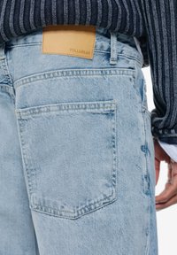 Világoskék farmernadrág klasszikus öt zsebes kialakítással. A derékrésznél a "PULL&BEAR" feliratú bőr címke található. Megkopott hatású.