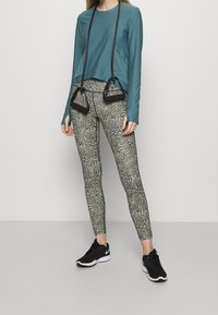 Teehlange Bluse mit Seiteneinsätzen, kombiniert mit Leggings im schwarz-weiß Tierdruck. Schwarze Sportschuhe runden das Outfit ab.