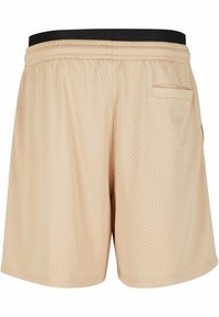 Shorts en mesh beige avec une ceinture élastique noire, comportant une poche arrière unique et une texture respirante pour un confort optimal.