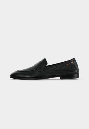 Zwarte leren penny loafer met lage hak, gestructureerd oppervlak en kleine meerkleurige vierkante stiksels nabij de hiel op een witte achtergrond.