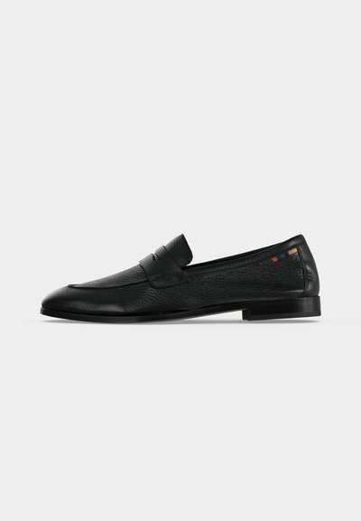 Μαύρο δερμάτινο penny loafer με χαμηλό τακούνι, υφή επιφάνειας και μικρό πολύχρωμο τετράγωνο ράψιμο κοντά στη φτέρνα σε λευκό φόντο.