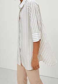 Witte en beige gestreepte button-up shirt met een relaxte pasvorm, voorzien van lange mouwen die bij de manchetten zijn opgerold en een gebogen zoom. Zachte stoftextuur.