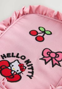 Rosa tygpåse med volangkanter. Broderade detaljer inkluderar "Hello Kitty", röda körsbär och en rosa rosett på en texturerad bakgrund.