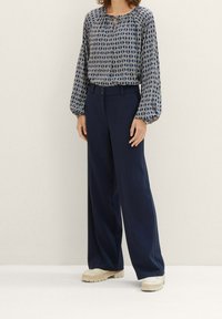 Blouse bleue à motifs avec manches ballon associée à un pantalon large bleu marine et des chaussures à plateforme crème. Tissu lisse et coupe décontractée.