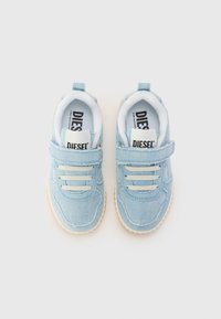 Baskets en denim bleu avec lacets blancs et bride en Velcro. Caractéristiques d'une tige texturée et d'une semelle en caoutchouc avec un bord de couleur claire. Étiquette de marque visible.