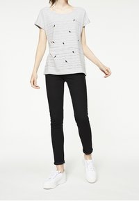 Top gris de manga corta con un ajuste relajado, que presenta un patrón de rayas horizontales y pequeños acentos oscuros. Combinado con jeans ajustados negros y zapatillas blancas.