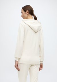 Κρεμ φούτερ με κουκούλα και απαλό ύφασμα, με κορδόνι στη κουκούλα, μακριά μανίκια και άνετη γραμμή. Ορατ ές ραφές στο τελείωμα.