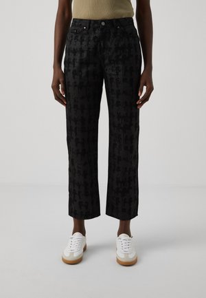 Zwarte cropped broek met een gestructureerd patroon, vijf zakken en riemlussen. Gecombineerd met witte sneakers met gumzolen.