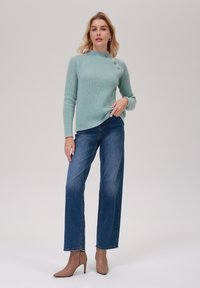 Pulover din tricot ribbed de culoare teal deschis, cu trei butoane decorative, asortat cu blugi largi de culoare albastră și cizme bej cu vârf ascuțit până la glezne.