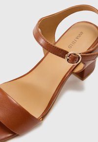 Brune lærhelsandaler med ankelrem og gylden spænde, bred frontrem og en struktureret inderside. Blokhæl design.