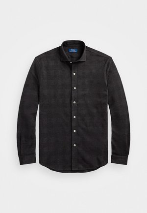 Chemise noire texturée à manches longues avec col et boutons blancs, posée à plat sur fond blanc.