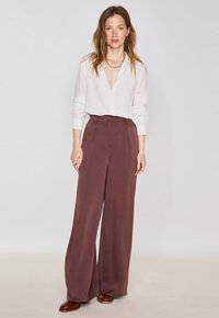 Camicia bianca a maniche lunghe con bottoni abbinata a pantaloni larghi color borgogna. Tessuto morbido con una vestibilità comoda, con pieghe frontali e vita alta.