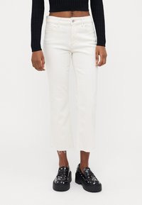 White cropped jeans with a straight leg and frayed hem, paired with black platform shoes featuring silver studs.