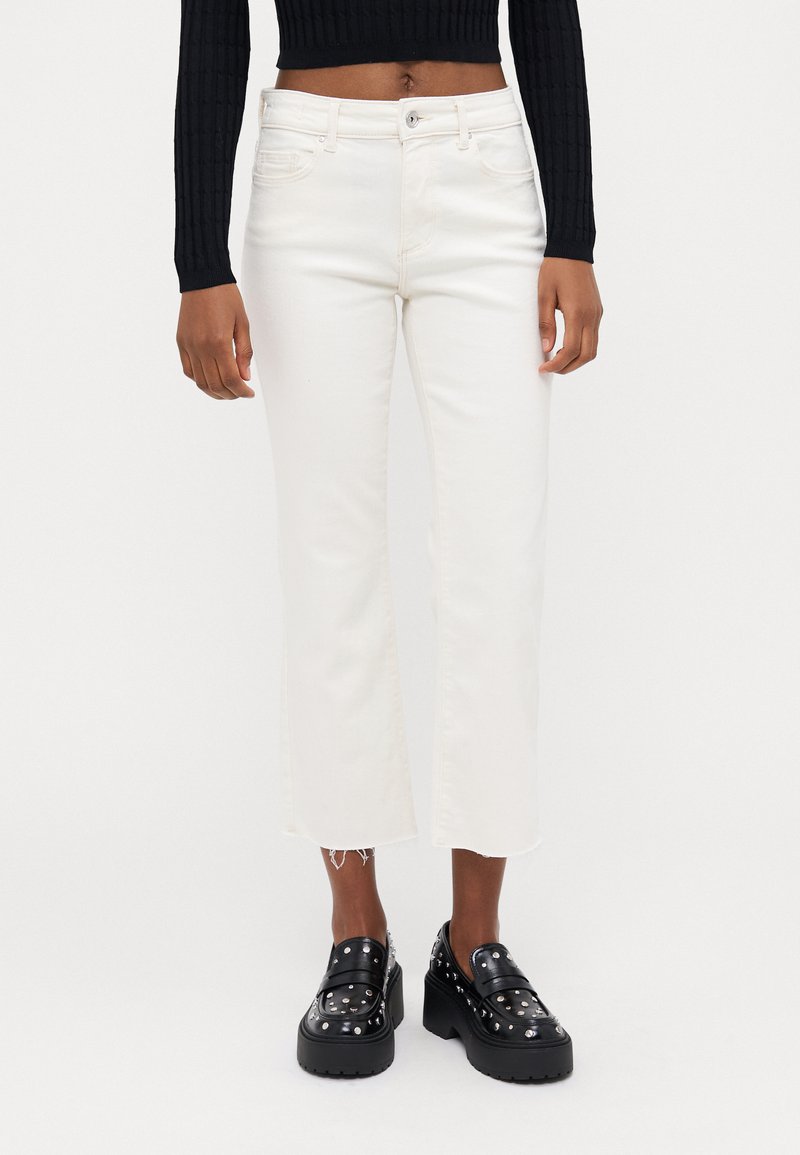White cropped jeans with a straight leg and frayed hem, paired with black platform shoes featuring silver studs.