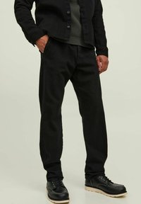 Pantalones negros de mezcla de algodón con forma cónica y bolsillos laterales. Combinados con una camisa negra abotonada y zapatos negros. Textura suave.
