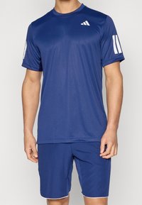 Granatowy koszulka sportowa z krótkimi rękawami, okrągłym dekoltem i białymi akcentami na rękawach. Wykonana z tkaniny odprowadzającej wilgoć. W zestawie szorty pasujące do koszulki.