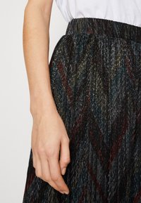 Tkaná černá sukně se vstřícnými kovovými nitěmi v barevném vzoru chevron, s nabíraným pasem a hladkou texturou.
