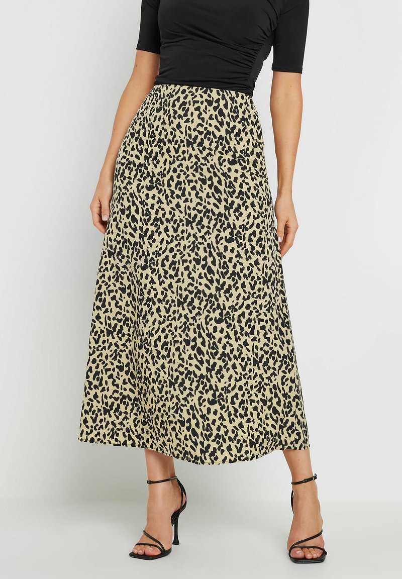 Jupe maxi imprimée léopard en beige et noir, avec un design fluide et une taille haute. Associée à des talons noirs à lanières.