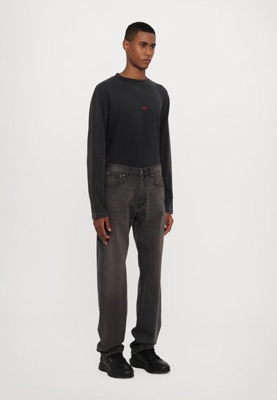 Crna majica dugih rukava s crvenim "424" logotipom, uparena s tamnosivim trapericama i crnim tenisicama. Glatka tkanina s opuštenim krojem.