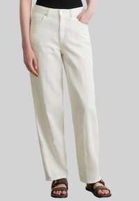 Białe, szerokie dżinsy wykonane z bawełny, z wysokim stanem, dwoma przednimi kieszeniami i zapięciem na guzik. Stylizowane z brązowymi sandałami.