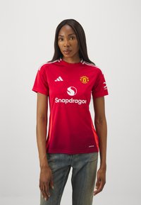 Rdeča majica Manchester United z kratkimi rokavi, okroglo ovratnikom, belimi črtami na ramenskih delih in logotipom "Snapdragon" na sprednji strani.