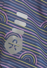 Flerfärgad tyg med horisontella ränder i blått, rosa och gult, med silverfärgad logotyp och cirkulära mönster. Slät textur.