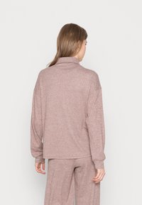 Pullover de malha rosa com colarinho alto, corte solto e textura canelada, acompanhado de calças a condizer, visto pela parte de trás.