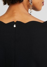 Černé šaty s hladkým výstřihem, středním zapínáním na zip s kovovým táhlem a hladkým texturovaným materiálem.