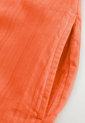 Gaiši oranžs audums ar smalku vertikālu svītru rakstu, ar sānu kabatu un maigu, teksturētu apdari. Redzamie šujmašīnas gali.