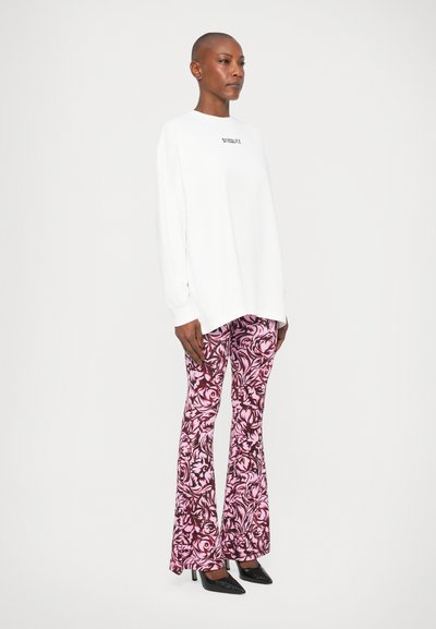 Cămașă albă cu mâneci lungi inscripționată cu textul "STYLE"; pantaloni evazați roz cu model floral; pantofi cu vârf ascuțit negri; material neted.