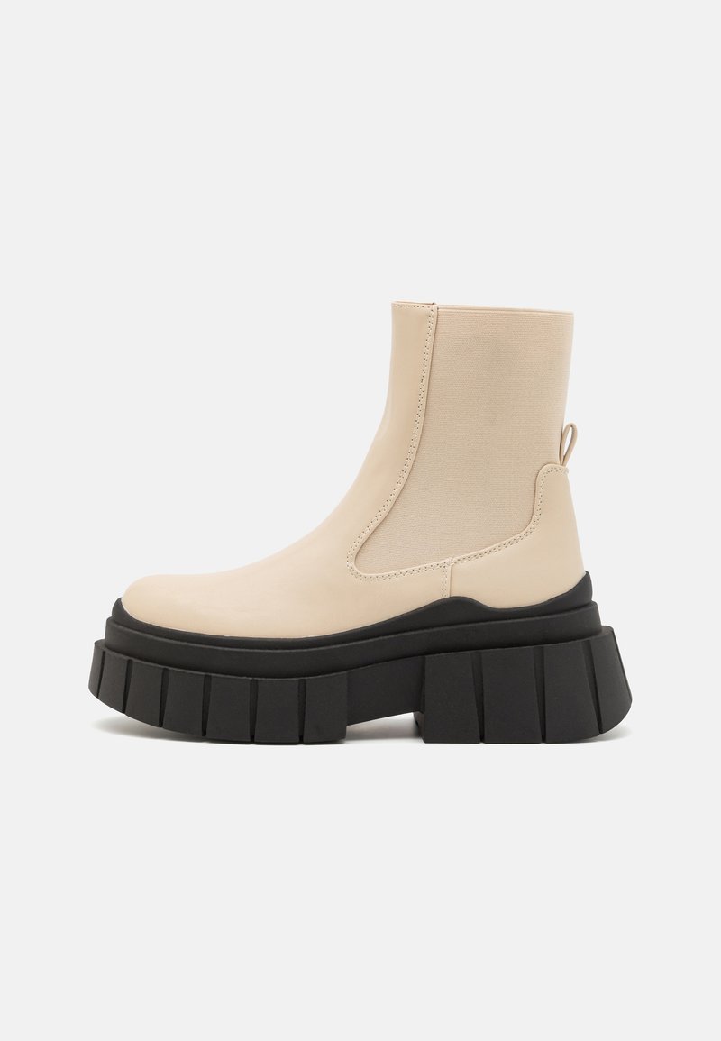 Beige ankle boot with elastic side panels and a pull tab. Thick black platform sole with ridged texture. Smooth leather upper and matte finish.