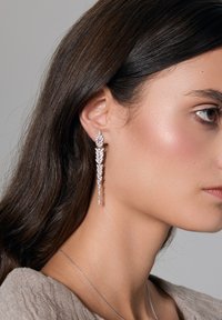 Srebrne kolczyki w formie wiszącej z wieloma błyszczącymi diamentami, z liściastym wzorem i wydłużonym kształtem. Teksturowane wykończenie, elegancki ogólny wygląd.