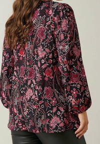 Blouse en tissu noir avec un motif floral dans des tons de rose et de rouge, manches froncées et coupe décontractée. Détail de surface texturée.