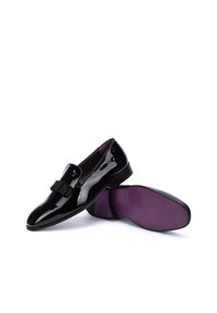 Mocasines de charol negro con detalle de lazo en la parte delantera, con un acabado suave y una plantilla morada. Suela de goma para mayor agarre.