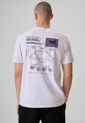 Mężczyzna z ogoloną głową w białej koszulce prezentujący na plecach wykres wzniesienia roweru górskiego oraz ilustracje rowerów.