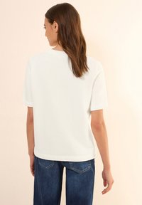 T-shirt blanc à manches courtes vu de dos, avec un col arrondi et une texture en coton lisse, associé à un jean en denim bleu.