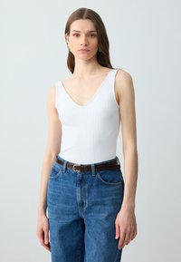 Body bianco a coste con scollatura a V profonda, abbinato a jeans in denim blu a vita alta e una cintura in pelle marrone. Dettagli di design semplici.