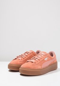 Baskets en suède rose avec une surface texturée, des lacets plats et une semelle en caoutchouc dotée d'un design nervuré. Logo latéral en blanc.