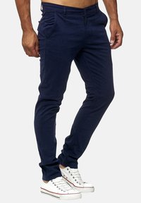 Mörkblå slim-fit byxor i en bomullsblandning, med framfickor, dragkedja och stylade med vita sneakers.