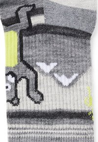 Grå stickade strumpor med en lekfull design som har ett svart motiv, vita accenter och klara gula höjdpunkter. Mjuk textur, längd till mitten av vaden.