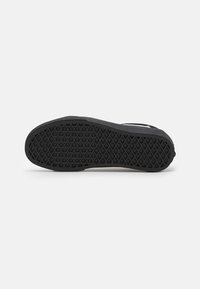 Suola di una sneaker nera che mostra motivi di trazione a diamante e circolari su uno sfondo bianco piano.