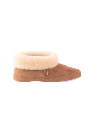 Tan suede slipper with a beige sheepskin cuff, rounded toe, and white rubber sole. Features a small leather tag on the side.