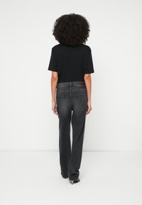 Melna īsroku blūze, saskaņota ar tumši pelēniem, platu kāju džinsiem, uz muguras jostasvietas ar zīmola uzliku un gludu tekstūru.