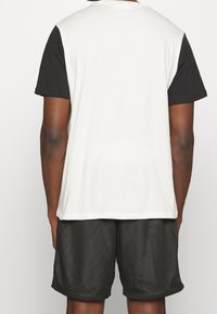 Tričko s krátkým rukávem, s černou spodní a bílou horní částí, vyrobené z bavlny. Síťované černé kraťasy s volným střihem a elastickým pasem.