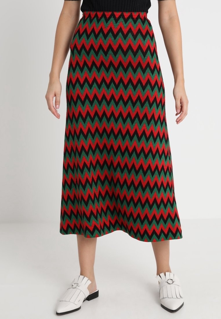 Knielanger Rock mit einem Zickzackmuster in Rot, Grün und Schwarz. Strickmaterial mit einem figurbetonten Bund, kombiniert mit weißen Slippern.