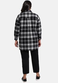 Chemise en flanelle à carreaux noir et blanc, à manches longues, avec un col et une coupe décontractée. Associée à un pantalon noir court et des chaussures à enfiler.