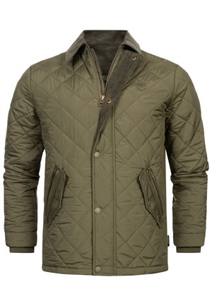 Chaqueta acolchada de color verde oliva con cuello alto, que presenta un cierre de cremallera frontal, dos bolsillos laterales en ángulo y puños acanalados. Detalles de pana en el cuello.