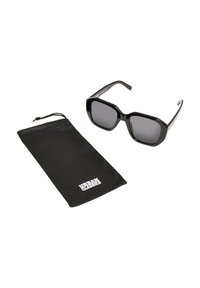 Fekete, oversized négyzet alakú napszemüveg szürke lencsékkel. Tartalmaz egy fekete puha tokot, amelyen az "URBAN CLASSICS" logó található. Sima felület, modern dizájn.