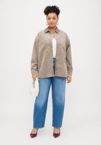 Rudas kordūrinis švarkas su mygtukų užsegimu, dviem krūtinės kišenėm, dėvimas virš baltos palaidinės, su mėlynomis tiesiomis džinsomis ir bordo bateliais.