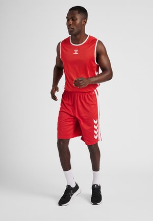 Röd sportig linne och shorts med vita detaljer och en logotyp. Svarta löparskor och vita strumpor fulländar den sportiga outfiten.